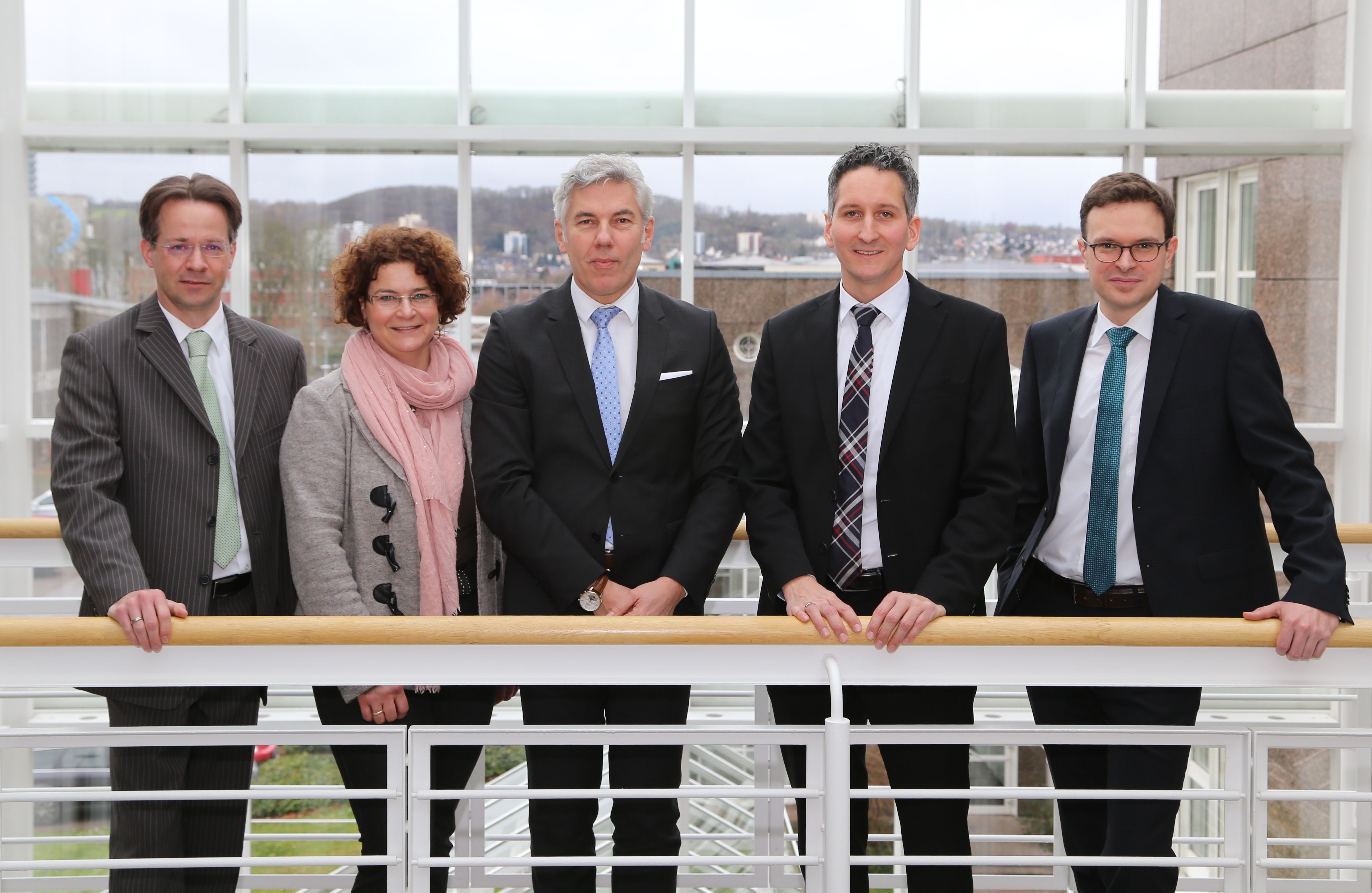 Vier Männer und eine Frau sind professionell gekleidet und stehen an einer Balustrade
